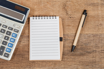 notebook showing empty page  and calculator on wooden desk