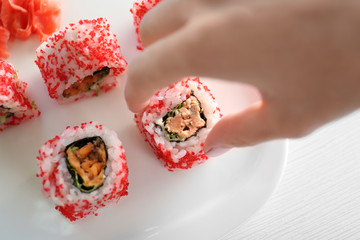 Female hand holding delicious sushi rolls on table