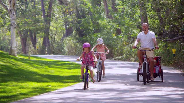Father riding bicycle with daughters and son