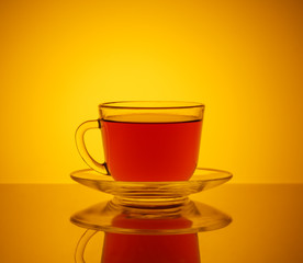 One transparent glass Cup . In the Cup of red drink. The Cup and saucer. The Studio photos. The rear light. The reflection on the table. The background orange.