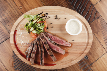Flank steak with salad and sauce on wooden surface