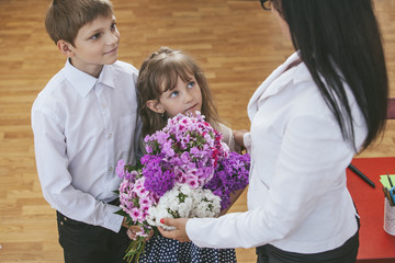 Boy and girl children give flowers as a school teacher