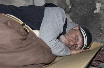 Homeless man sleeping on cardboard and an old sleeping bag out on the streets 