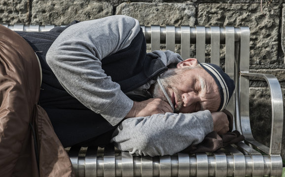 Homeless man sleeping with old blankets on a park bench 