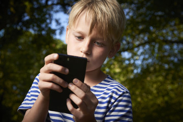 Child young boy with mobile phone outdoor. Child looking at the screen, playing, using apps. Boy playing with smartphone.