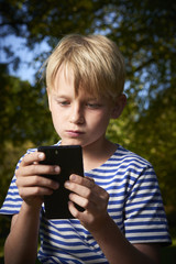 Child young boy with mobile phone outdoor. Child looking at the screen, playing, using apps. Boy playing with smartphone.