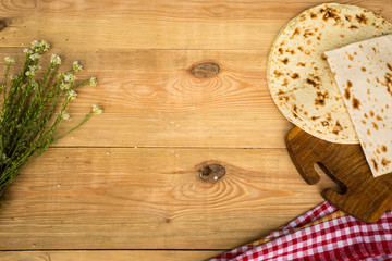 Checkered napkin, pita bread and cute white wildflowers on wooden background. Place for text. Top view.