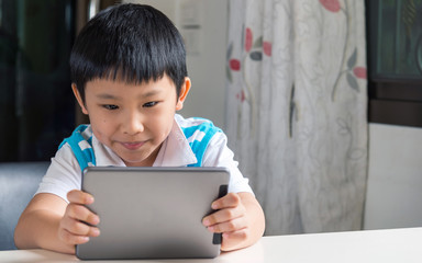 Young happy asian boy sitting , he browses the internet on a tablet computer at home.