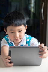 Young asian boy sitting , he browses the internet on a tablet computer at home.