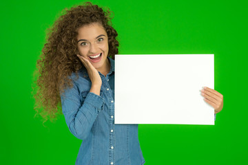 The young woman show empty sheet of paper the green background