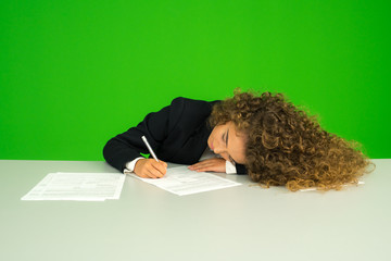 The young girl lie at the desk and write on the green background