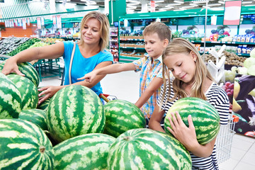 Mom with kids choose watermelon at grocery store