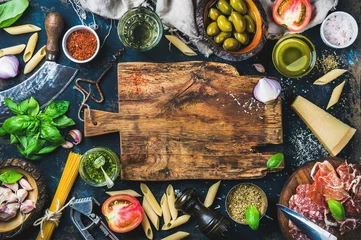 Fototapete Küche Italienische Lebensmittelkochzutaten auf dunklem Hintergrund mit rustikalem Holzschneidebrett in der Mitte, Draufsicht, Kopierraum
