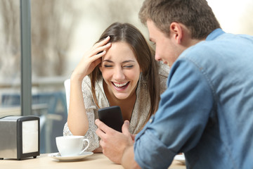 Couple laughing watching media in smart phone