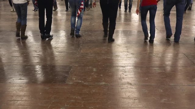 Legs of people dancing together western dance at a country folk festival wearing cowboy boots, jeans and USA flag. Music, traditions and fun. Learning line dance
