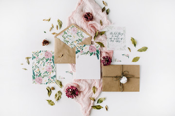 Workspace. Wedding invitation cards, craft envelopes, pink and red roses and green leaves on white...