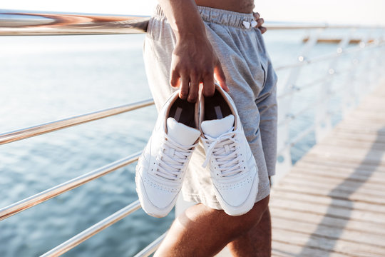 Cropped image of sportsmen hands holding sneakers at pier