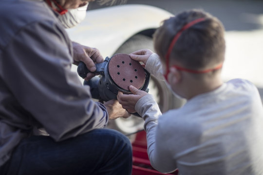 Senior man and boy looking at grinding machine at car