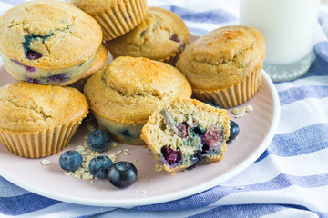 Closeup image of oatmeal blueberry muffins on a plate with a glass of milk placed on a blue tablecloth.