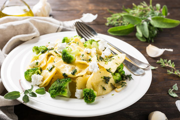 Plate of ravioli with broccoli, goat cheese and herbs on old wooden background. Italian healthy food concept.