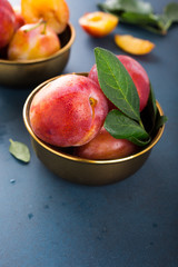 Fresh plums in bronze bowl on blue stone background. Selective focus. Healthy food concept. Copy space.