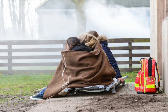 Kinder sitzen in eine Decke geh&uuml;llt vor einem brennenden Haus