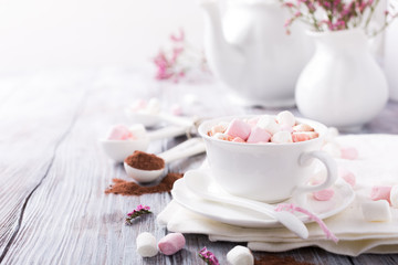 Cup of hot chocolate with mini marshmallows with cocoa on white wooden background with copy space.