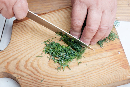Female hands chopping dill on wooden board.