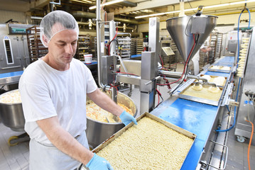 Mann stellt Kuchen in einer Großbäckerei am Fliessband her // man presents cakes in a bakery on...