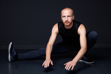 Fototapeta na wymiar Fitness man performing legs stretching, dark background
