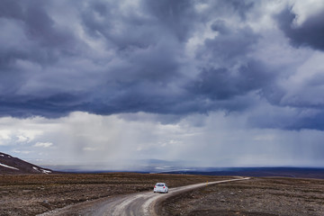 dramatic landscape from Iceland, car on the remote road, wilderness and moody sky