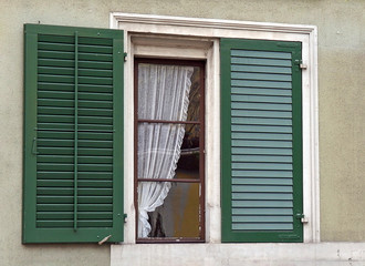 house window with green shutters and lace curtain