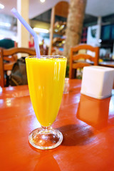 Juice in the misted over glass on wooden table on the blurred cafe background. Fresh yellow smoothie with mango.