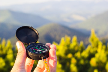 Hand holding compass on summer mountains background