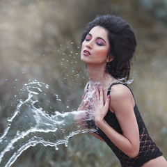 Beautiful brunette in a spray of water outdoors.