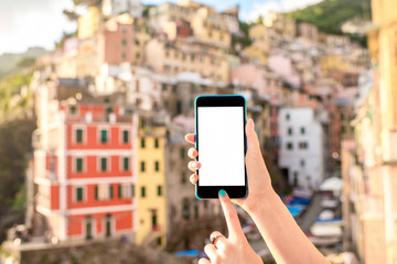 Naklejka premium Holding smart phone with white screen on the old italian town background in Riomaggiore