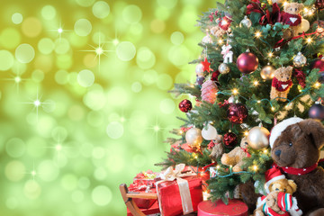 Christmas tree with decoration, gifts and teddy bears on green bokeh background with blurred lights and shining stars.