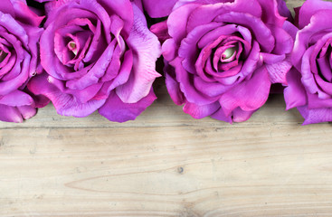 Border with artificial pink roses isolated on wooden background.