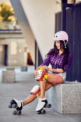 Active lifestyle girl is going to ride on roller skates. Beautiful girl puts protection equipment for rollerblading. Attractive teenager sitting on street a sunny day.