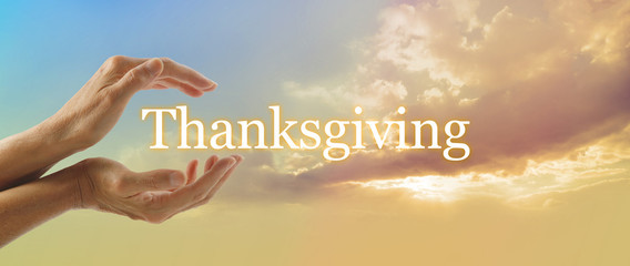 Celebrate Thanksgiving - Female hands cupped with the word THANKSGIVING floating between on a warm golden cloud background with blue sky in top left corner and copy space - obrazy, fototapety, plakaty