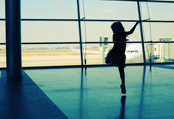 Fototapeta na wymiar Silhouette of cute girl jumping in front of the window in airpor