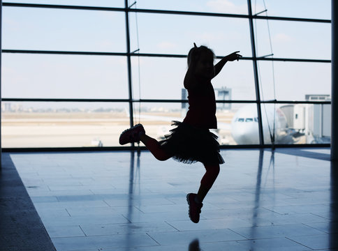 Silhouette of cute girl jumping in front of the window in airpor