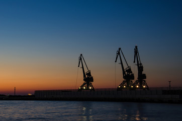 Fototapeta premium PORT CRANES AT NIGHT. Cruise Ship Terminal in Gdynia. Outline of port cranes at dawn. 