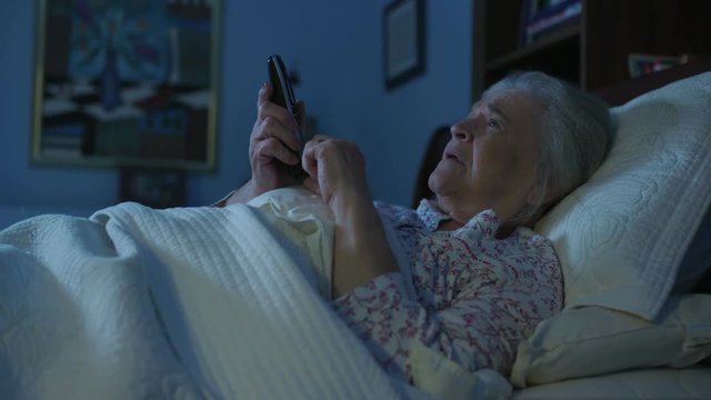 An elderly senior woman in bed struggles with Alzheimer's or dementia, and can't remember the phone number. Shot in 4K UHD.