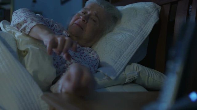 An elderly senior woman in bed is having a medical emergency and tries to reach her telephone. Shot in 4K UHD.