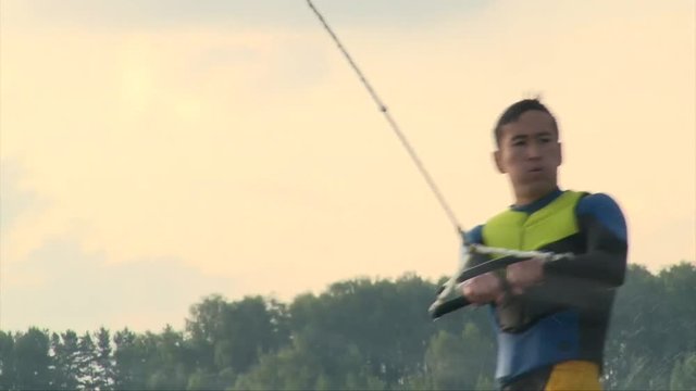 Close up shot of wakeboarder man in diving suit riding the wave and crush in water, summer sunset on the lake