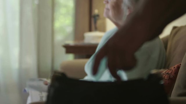 A senior elderly woman watches TV as a hand steals a wallet from her purse. Shot in 4K UHD.
