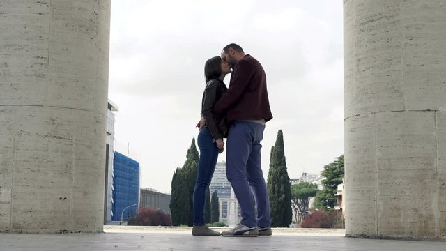 Young couple in love hugging and kissing near columns in city 
