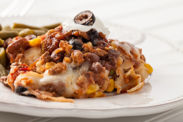 Fiesta bake Mexican lasagna with corn tortillas, pinto beans, olives, corn, tomatoes, and sour cream served with green beans close up shot