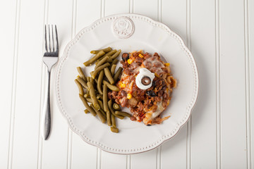 Fiesta bake Mexican lasagna with corn tortillas, pinto beans, olives, corn, tomatoes, and sour cream served with green beans top view 